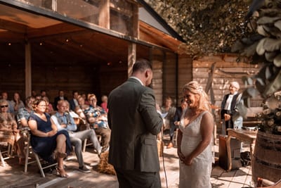 Rob spreekt zijn geloften uit terwijl Tamara ontroerd luistert en de gasten onder de veranda toekijken